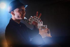 Magician showing trick with playing cards. Magic or dexterity, circus, gambling. Prestidigitator in dark room with fog photo