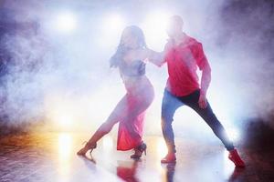 hábiles bailarines actuando en la habitación oscura bajo la luz y el humo del concierto. pareja sensual realizando una danza contemporánea artística y emocional foto