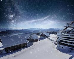 Night with stars. Christmas landscape. Wooden house in the mountain village. Night landscape in winter photo