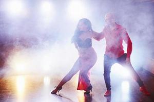 hábiles bailarines actuando en la habitación oscura bajo la luz y el humo del concierto. pareja sensual realizando una danza contemporánea artística y emocional foto