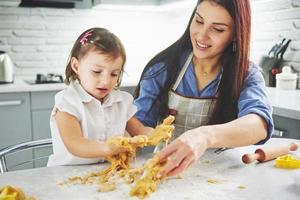 Happy family in the kitchen. Holiday food concept. Mother and daughter preparing the dough, bake cookies. Happy family in making cookies at home. Homemade food and little helper photo