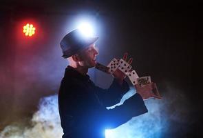 Magician showing trick with playing cards. Magic or dexterity, circus, gambling. Prestidigitator in dark room with fog photo