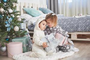 Two little sister girls open their gifts at the Christmas tree in the morning on the deck photo