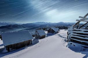 noche con estrellas. paisaje navideño. casa de madera en el pueblo de montaña. paisaje nocturno en invierno foto