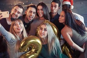 Group beautiful young people doing selfie in the new year party, best friends girls and boys together having fun, posing lifestyle people concept. Hats santas and champagne glasses in their hands