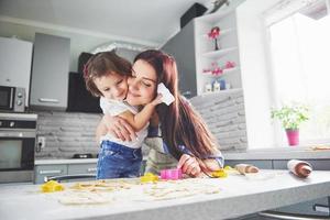 Happy family in the kitchen. Holiday food concept. Mother and daughter preparing the dough, bake cookies. Happy family in making cookies at home. Homemade food and little helper photo