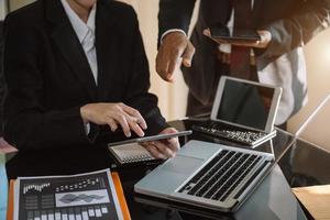 mano de hombre de negocios usando laptop y tableta con diagrama de red social y dos colegas discutiendo datos en el escritorio como concepto a la luz de la mañana. foto