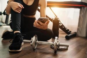 Close up of woman using smart phone while workout in fitness gym. Sport and Technology concept. Lifestyles and Healthcare theme.