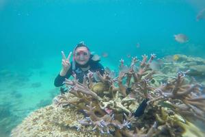 Happy woman snorkeling underwater and posing with a coral reef and fish photo