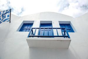 balcón de la casa tradicional blanca de Grecia con ventanas azules y bandera griega foto