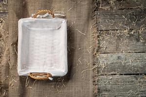 Empty wicker bread basket with white napkin on burlap cloth covered with straw photo