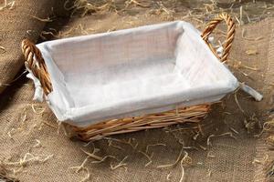 Empty wicker bread basket with white napkin on burlap cloth covered with straw photo