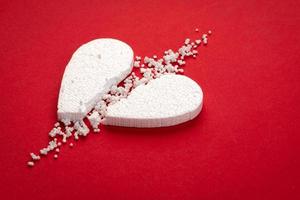 White broken styrofoam heart on a red paper background close up