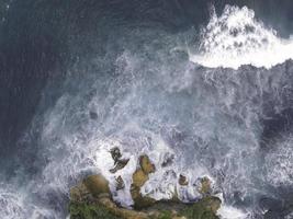 vista aérea de arriba hacia abajo de las olas gigantes del océano rompiendo y haciendo espuma en la playa de coral foto