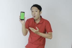 Wow face of Young asian man smiling when showing green screen of smartphone in studio background photo