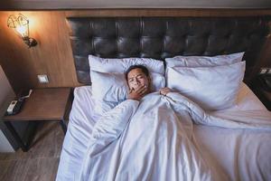 Asian man using blanket yawning while lying on a bed photo