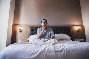 Asian man using blanket yawning while sitting on a bed photo