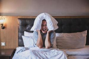 Insomnia man screaming disturbed with covering his ears use a pillow on a bed photo