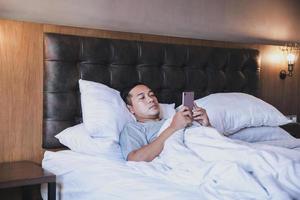 Men using smartphone while lying on the bed using a blanket photo