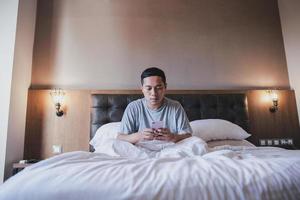 Man sitting and using a phone on the bed before going to sleep photo