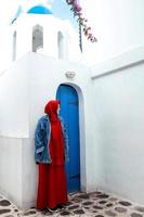 mujer musulmana posando en la puerta de madera azul tradicional de santorini y cúpulas azules foto