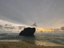 puesta de sol en el mar entre olas y rocas en indonesia foto