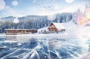 Blue ice and cracks on the surface of the ice. Frozen lake in winter mountains. It is snowing. The hills of pines. Winter. Carpathian Ukraine Europe photo