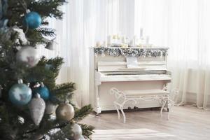 decoración de año nuevo. árbol de navidad cerca de piano blanco en el fondo de la ventana foto