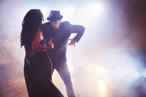 hábiles bailarines actuando en la habitación oscura bajo la luz y el humo del concierto. pareja sensual realizando una danza contemporánea artística y emocional foto