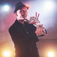 Magician showing trick with playing cards. Magic or dexterity, circus, gambling. Prestidigitator in dark room with fog photo