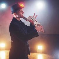 Magician showing trick with playing cards. Magic or dexterity, circus, gambling. Prestidigitator in dark room with fog photo