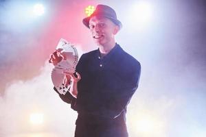 Magician showing trick with playing cards. Magic or dexterity, circus, gambling. Prestidigitator in dark room with fog photo