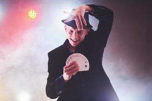 Magician showing trick with playing cards. Magic or dexterity, circus, gambling. Prestidigitator in dark room with fog photo