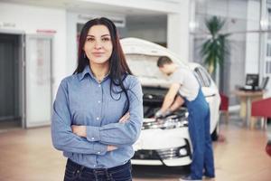 mujer en un garaje de automóviles recibiendo servicio mecánico. el mecánico trabaja bajo el capó del coche foto