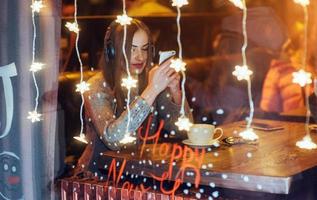 hermosa mujer joven sentada en la cafetería, bebiendo café. modelo escuchando música. navidad, feliz año nuevo, día de san valentín, concepto de vacaciones de invierno foto