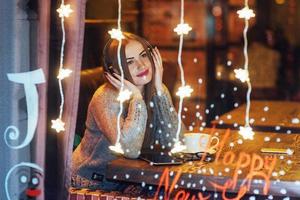 Young beautiful woman sitting in cafe, drinking coffee. Model listening to music. Christmas, Happy new year, Valentines day, winter holidays concept photo