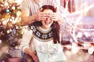 Young couple celebrating Christmas. A man suddenly presented a present to his wife. The concept of family happiness and well-being. Bokeh light soft effect