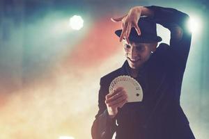 Magician showing trick with playing cards. Magic or dexterity, circus, gambling. Prestidigitator in dark room with fog photo