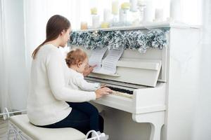 mira desde atrás a la madre y la hija tocando el piano blanco