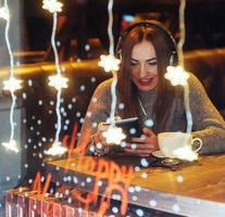 hermosa mujer joven sentada en la cafetería, bebiendo café. modelo escuchando música. navidad, feliz año nuevo, día de san valentín, concepto de vacaciones de invierno foto