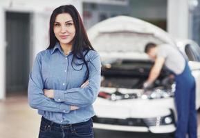 Woman at a car garage getting mechanical service. The mechanic works under the hood of the car photo