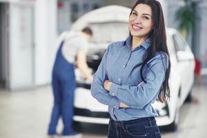 Woman at a car garage getting mechanical service. The mechanic works under the hood of the car photo