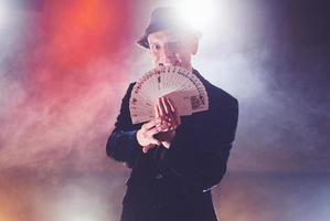 Magician showing trick with playing cards. Magic or dexterity, circus, gambling. Prestidigitator in dark room with fog photo