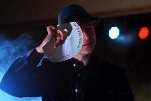 Magician showing trick with playing cards. Magic or dexterity, circus, gambling. Prestidigitator in dark room with fog photo