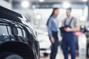 Beautiful young woman is talking to handsome car mechanic while repair a car in dealership photo