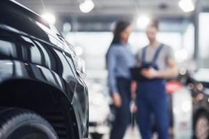 Beautiful young woman is talking to handsome car mechanic while repair a car in dealership photo