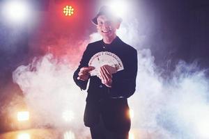 Magician showing trick with playing cards. Magic or dexterity, circus, gambling. Prestidigitator in dark room with fog photo