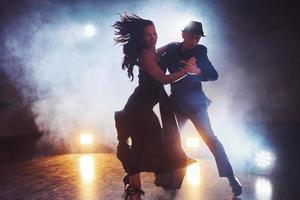 hábiles bailarines actuando en la habitación oscura bajo la luz y el humo del concierto. pareja sensual realizando una danza contemporánea artística y emocional foto