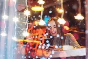 hermosa mujer joven sentada en la cafetería, bebiendo café. modelo escuchando música. navidad, feliz año nuevo, día de san valentín, concepto de vacaciones de invierno foto