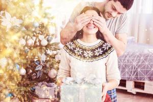 Young couple celebrating Christmas. A man suddenly presented a present to his wife. The concept of family happiness and well-being. Bokeh light soft effect photo